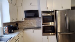 A kitchen with white cabinets, a stainless steel refrigerator, a microwave, and two ovens. - Ida's Oasis  near JRMC Hospital ,  Pine Bluff Country Club & Restaurants . (Pine Bluff)