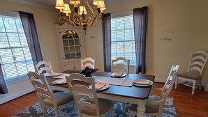 A dining room with a chandelier, white chairs, a table, and a patterned rug. - Ida's Oasis  near JRMC Hospital ,  Pine Bluff Country Club & Restaurants . (Pine Bluff)