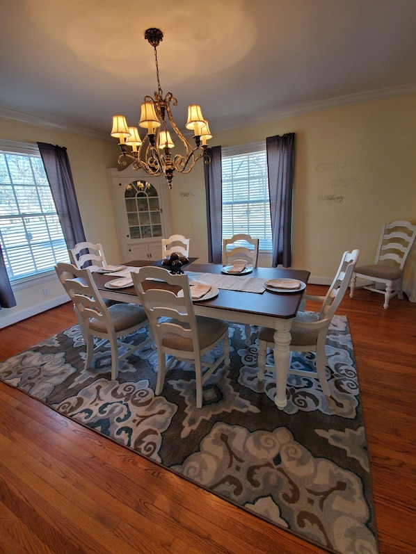 A dining room with a chandelier, white chairs, a table, and a patterned rug.