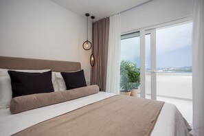 A modern hotel room with a large bed, a potted plant, and a view of the sea.