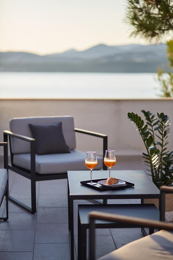 A terrace with a table and a chair, two glasses of a beverage, and a croissant on a tray.