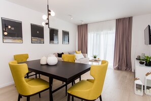 A modern dining area with a black table and yellow chairs, a sofa with cushions, and a TV on the wall.