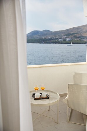 A balcony with a table set for two, overlooking a body of water and hills. - Guest House Blanka (Okrug)