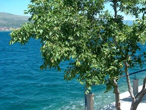 A tree-lined view of a coastal area with a clear blue sea and a distant landmass. - Guest House Blanka (Okrug)