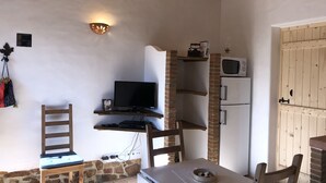 Une pièce chaleureuse avec une télévision posée sur une étagère en bois, un mur en pierre, une chaise en bois et une table sur laquelle se trouve un bol.