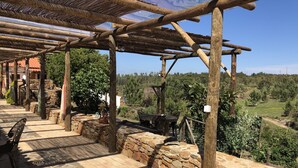 Une terrasse dallée de pierres, agrémentée d’une pergola en bois, de murs en pierre et offrant une vue sur un paysage verdoyant.