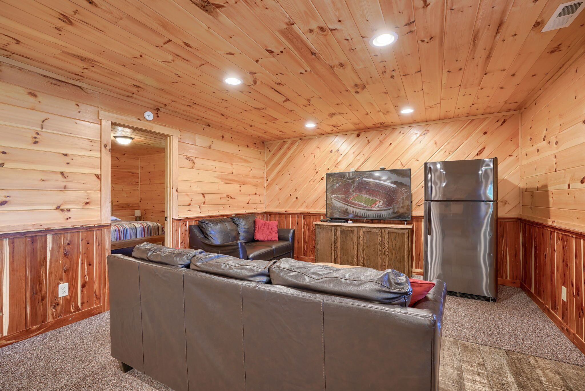 Een gezellig cabin interieur met een houten plafond, een bank, een koelkast en een televisie op een houten kast.