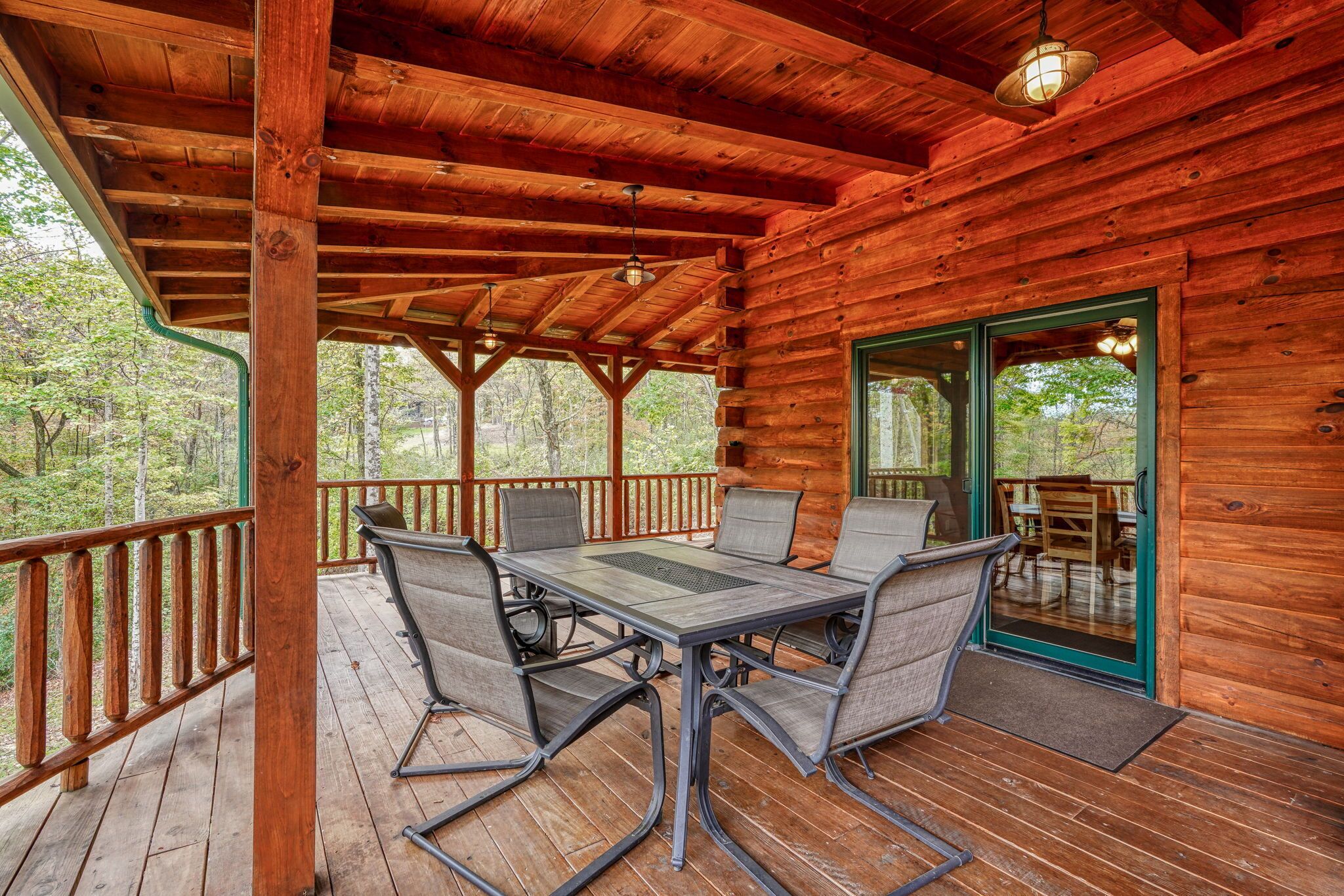 A wooden deck with a table and chairs, a covered area with a wooden ceiling, and a glass door leading to an outdoor area.