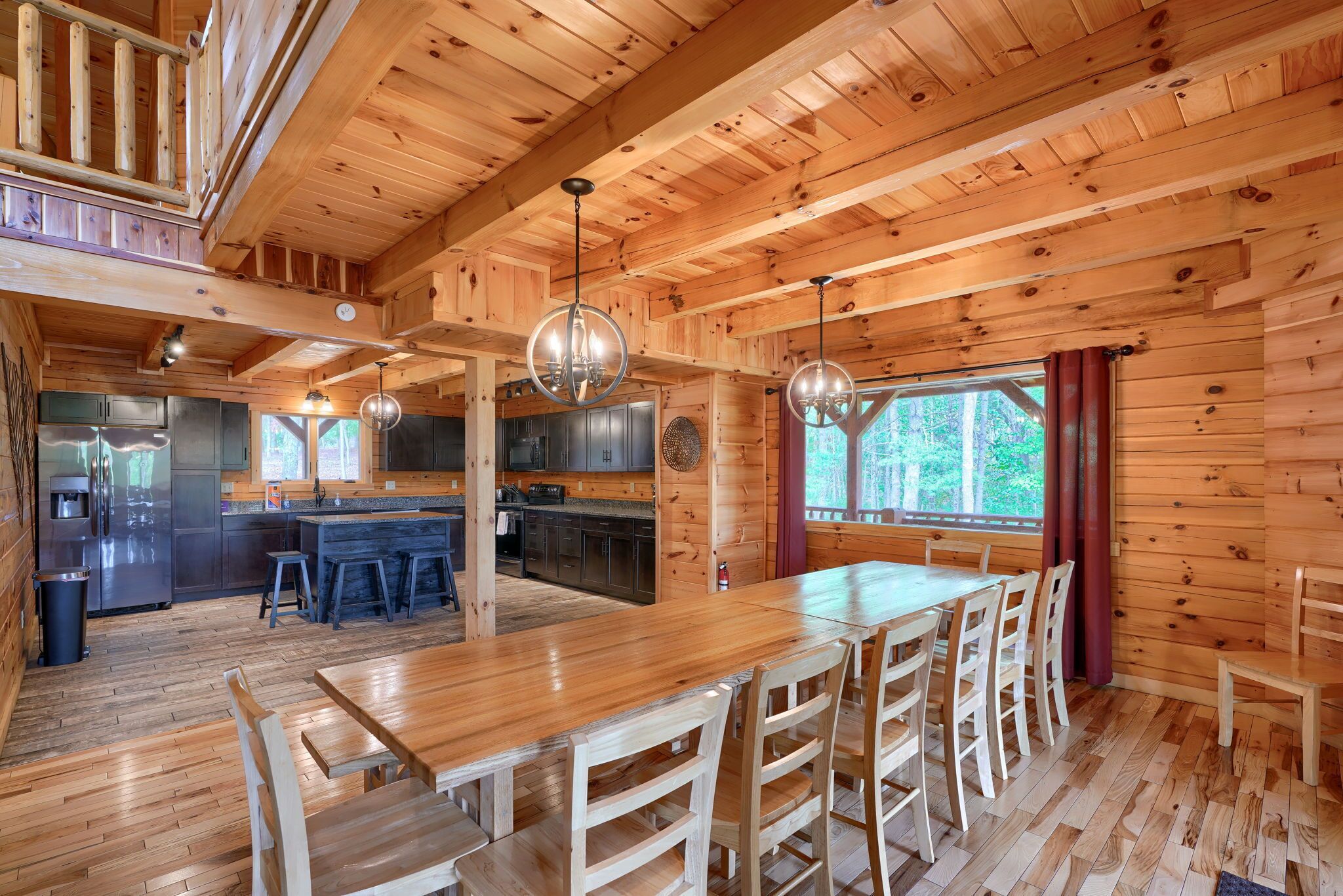 Una cabaña de madera espaciosa con una gran mesa y sillas de comedor, un área de cocina y un balcón.