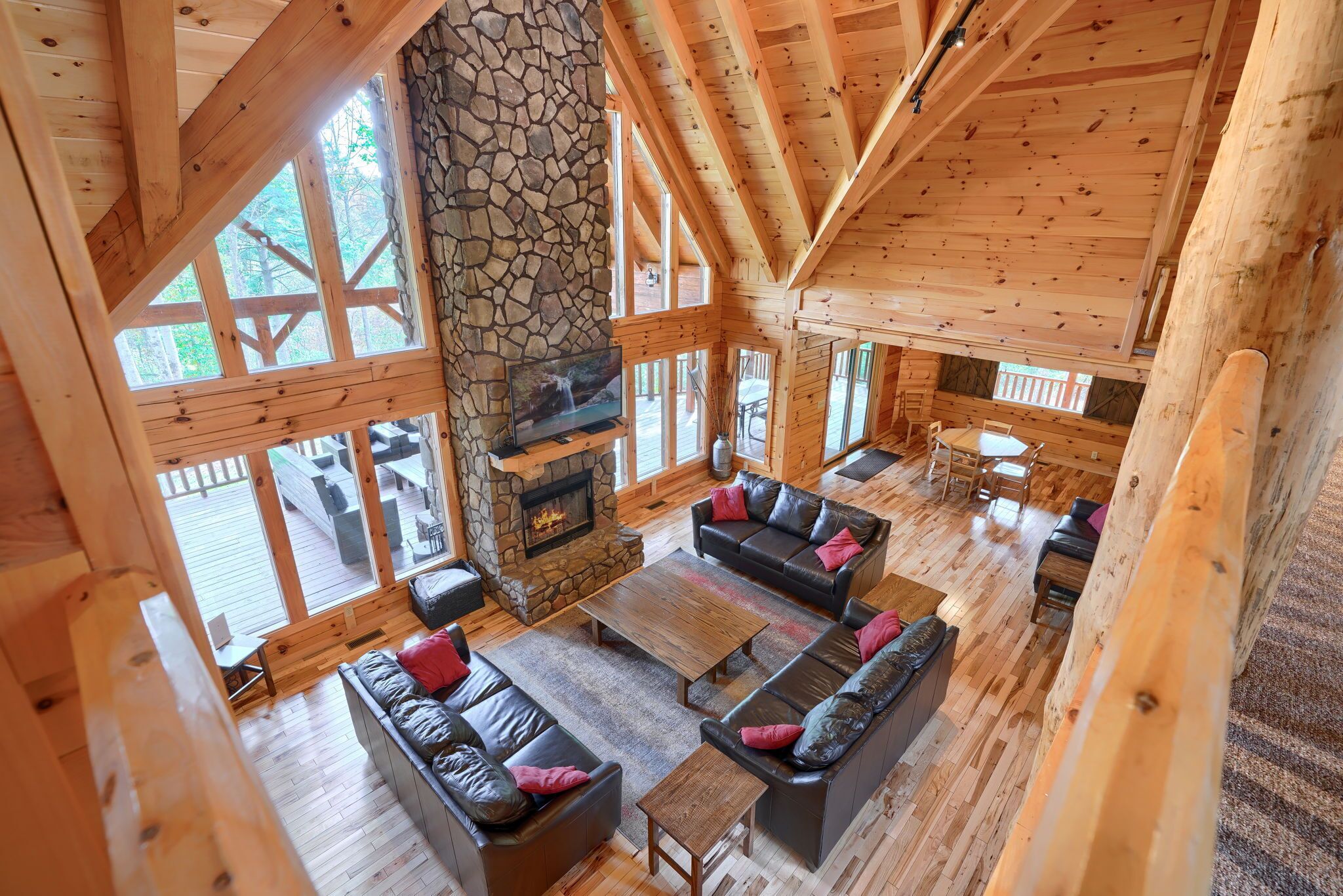 Interior espacioso de una cabaña de madera con chimenea de piedra, muebles de madera y ventanas amplias.