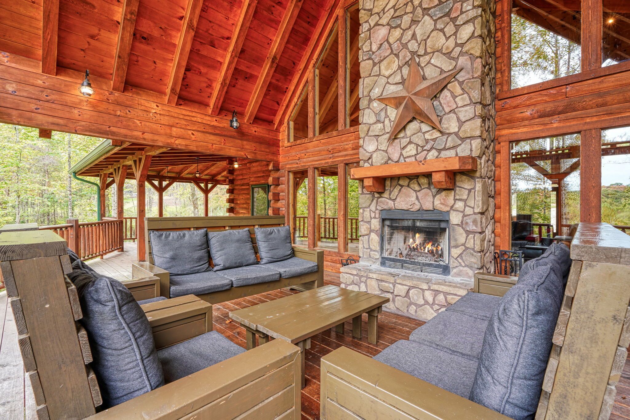 A log cabin with a stone fireplace, wooden furniture, and a deck overlooking a forest.