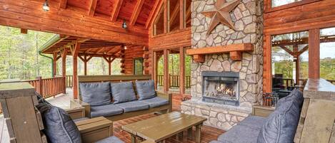 A log cabin with a stone fireplace, wooden furniture, and a deck overlooking a forest.