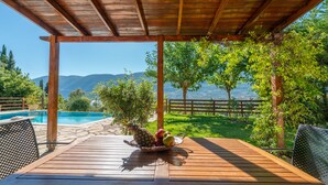 A wooden deck with a pool, fruit basket, and a view of mountains. - Melissi Villa, overlooking Vasiliki bay, close to the beach and other amenities! (Lefkada)