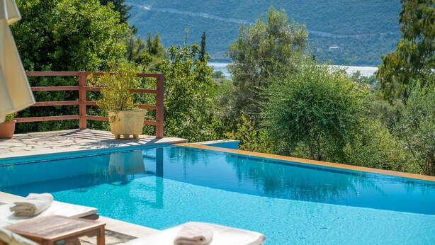 A swimming pool with lounge chairs and a wooden deck. - Melissi Villa, overlooking Vasiliki bay, close to the beach and other amenities! (Lefkada)
