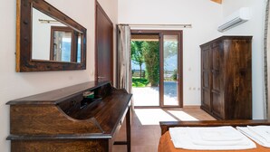 A bedroom with a wooden dresser, a large mirror, a bed with white linens, and a view of the outdoors through a sliding glass door. - Melissi Villa, overlooking Vasiliki bay, close to the beach and other amenities! (Lefkada)