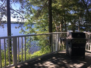 A deck with a grill and a view of a lake surrounded by trees.