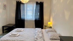 A hotel room with a bed, a bedside table with a lamp, a window with curtains, and a wall sign. - Amazing Villa Littau  (Luzern)
