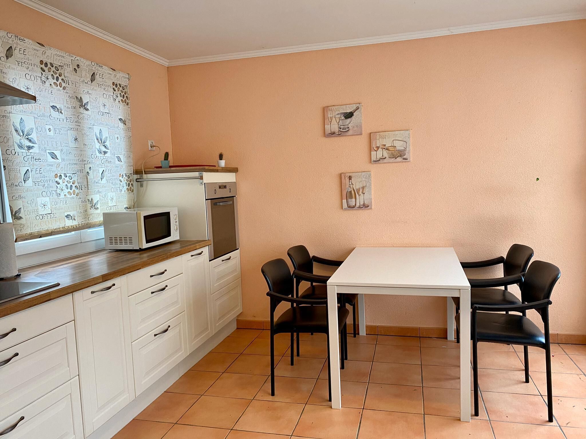 A compact kitchen with white cabinets, a microwave, an oven, and a dining table with four chairs.