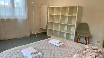 A hotel room with a bed, a wardrobe, a chair, and a window with sheer curtains.