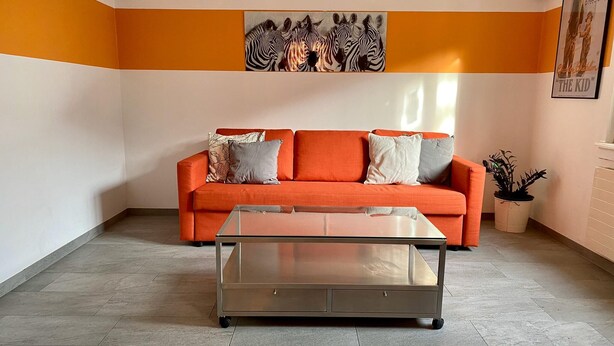 A living room with an orange sofa, a glass coffee table, and a zebra painting on the wall. - Amazing Villa Littau  (Luzern)