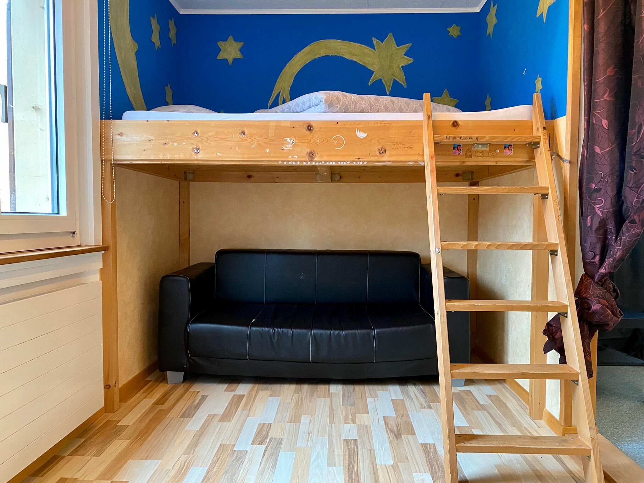 Un lit superposé avec une échelle, un canapé noir et un mur décoré de motifs en forme d’étoiles.
