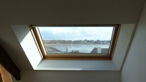 Ein Dachfenster in einem Zimmer mit Blick auf ein Gewässer und eine entfernte Küstenlinie.