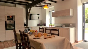 A kitchen with a dining table set for breakfast, a microwave, an oven, and a hanging light fixture.