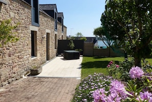 A stone building with a paved patio, outdoor seating, and a garden with flowers.