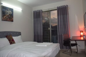 A hotel room with a bed, a desk, a chair, a window with curtains, and a painting on the wall. - Fairmont Guest House (Dhaka)