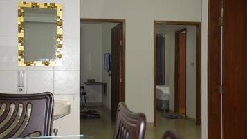 A room with a dining table, chairs, a mirror with a decorative frame, and a doorway leading to another room.