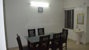 A dining area with a glass table and black chairs, a white sink, and a window with bars. - Fairmont Guest House (Dhaka)