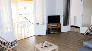 A living room with a TV on a wooden stand, a small table, and a sofa. - Near Royan, 96m2 house with 500m2 enclosed garden - 3 beaches within 600m (Vaux-sur-Mer)