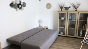 A minimalist bedroom with a bed, a nightstand, a lamp, a clock, and a cabinet with glass doors. - Near Royan, 96m2 house with 500m2 enclosed garden - 3 beaches within 600m (Vaux-sur-Mer)