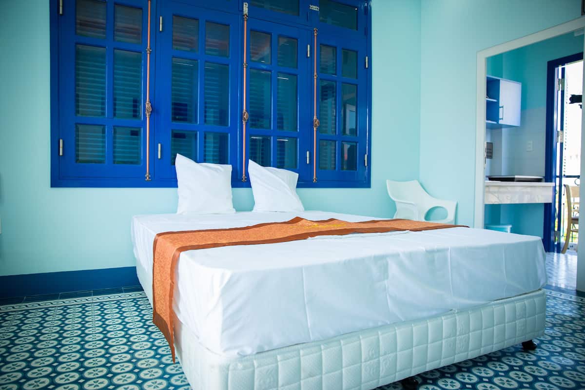 A room with a bed, a window with blue shutters, and a patterned floor.