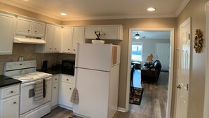 A kitchen with white cabinets, a stove, and a refrigerator. There is a dining area visible in the background. - Parris Island Marine Corps Graduation PCS Orders Travel Nurses Beaufort Home (Beaufort)