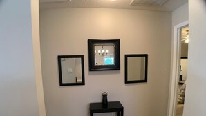 A hallway with a wooden floor, a black console table, and three framed mirrors on the wall. - Parris Island Marine Corps Graduation PCS Orders Travel Nurses Beaufort Home (Beaufort)