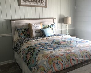 Un letto con copriletto a motivi floreali e diversi cuscini, tra cui uno con decorazioni a tema spiaggia.