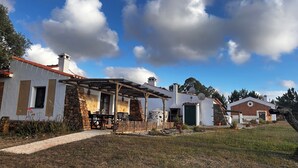 Une maison de campagne avec un patio couvert, des murs en pierre et une cheminée en briques.