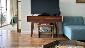 Un soggiorno con una TV a schermo piatto su un supporto in legno, un divano blu e un piccolo tavolino con una pianta.