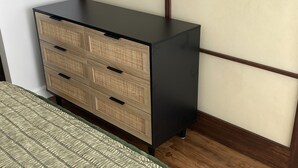 Una stanza con un letto, una cassettiera di legno e una parete semplice.