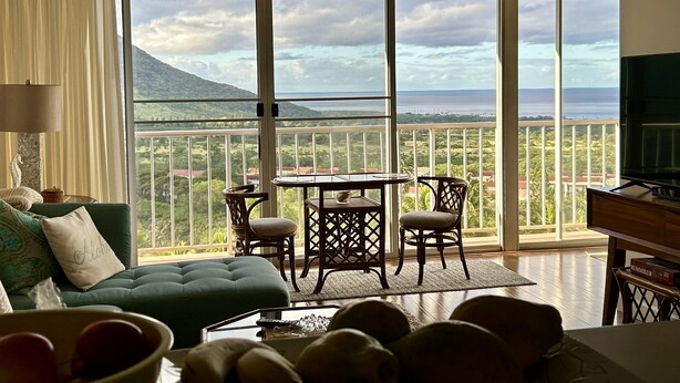 Un soggiorno con divano, tavolo e sedie, televisione, e un balcone con vista sul mare e sulle montagne.