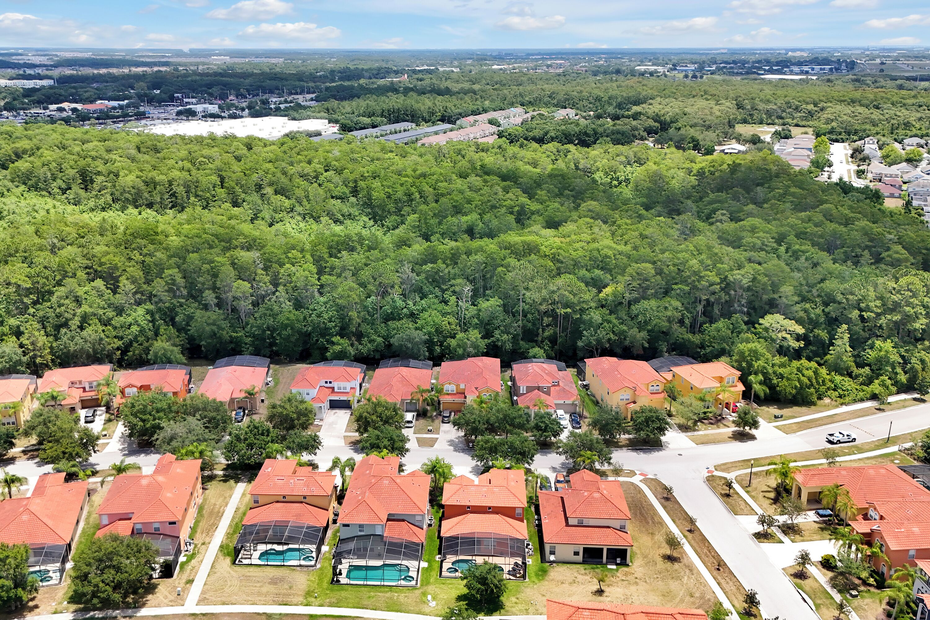Un quartier résidentiel avec des maisons aux toits rouges, une piscine et une forêt dense en arrière-plan.
