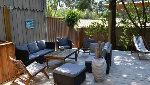 Une terrasse extérieure avec une plateforme en bois, un canapé, une table à manger, une chaise et un grand vase décoratif.