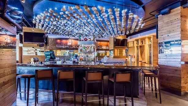 A bar area with wooden walls, a curved ceiling with hanging lights, and a bar counter with stools. - Quiet Village Monache Retreat | Balcony Views, Fireplace, Walk to Gondola (Mammoth Lakes)
