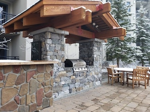 An outdoor barbecue area with a stone wall and wooden pergola. - Quiet Village Monache Retreat | Balcony Views, Fireplace, Walk to Gondola (Mammoth Lakes)