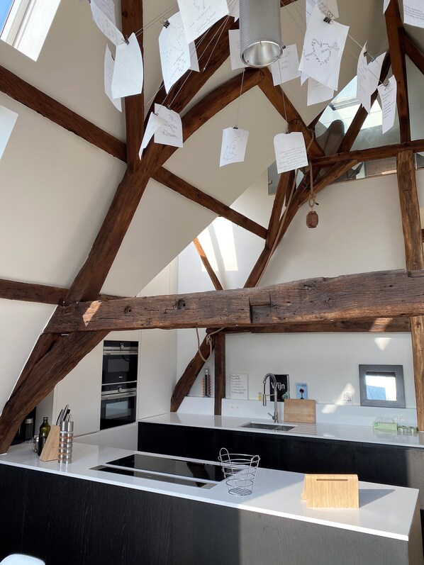 A kitchen with a wooden ceiling, a white countertop, and various kitchen utensils. - Sleeping in Medieval Ghent (Gent)