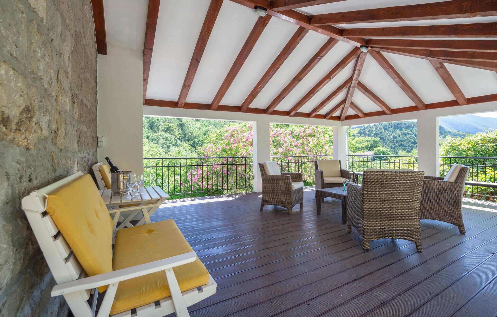 A covered outdoor seating area with wicker furniture and a table, overlooking a lush landscape.