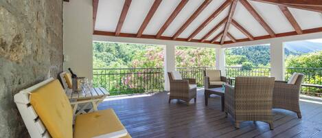 A covered outdoor seating area with wicker furniture and a table, overlooking a lush landscape.
