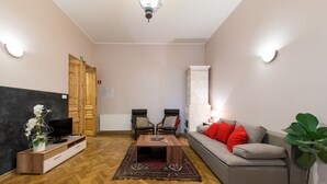 Een woonkamer met een bank, twee stoelen, een salontafel, een televisie, een open haard en een plant.