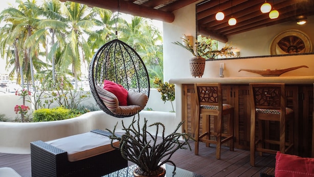 Un fauteuil suspendu avec un coussin, une table en bois avec une plante, et un coin bar avec des chaises en bois et un bol décoratif.